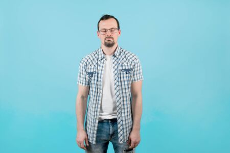 a man in a plaid shirt with bristles in glasses stands in a very relaxed position with his eyes closed. He is very tired and sleeps on the go.の写真素材