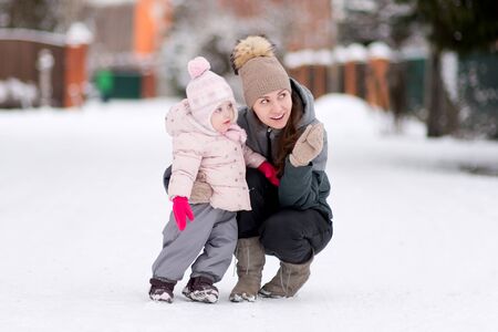 A young mother points at something to her little daughter, with whom she walks through a snowy village on a winter morningの写真素材