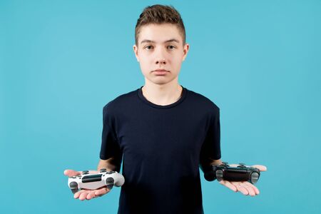 A teenager in a blue T-shirt with a calm face holds two joysticks in his hands. White and black...