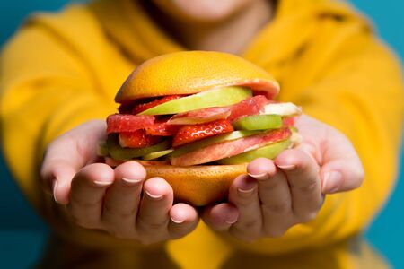 a vegetarian burger of fresh fruits and berries lies on the palms of the girl, close upの写真素材