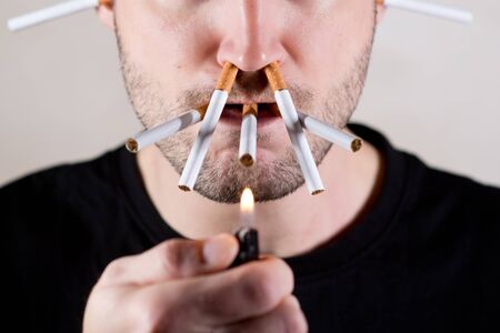 the lower half of the unshaven face of a man and a lot of cigarettes in his mouth and nose, close upの写真素材