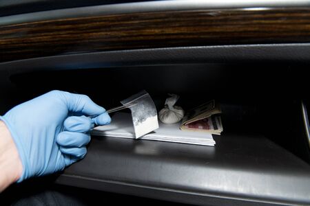 a gloved hand takes out tweezers cocaine from the glove compartment of a car. Styling for...