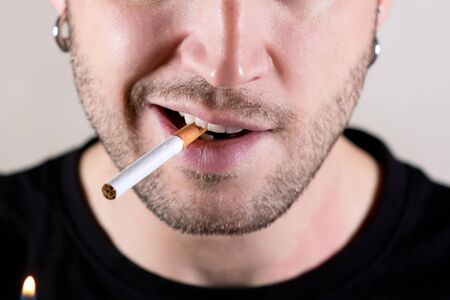 lower half of the face of an unshaven pierced man who is about to light a cigaretteの写真素材