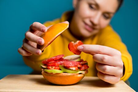 girl puts a piece of strawberry in a grapefruit burger in which sliced fruits and berries lie, close upの写真素材
