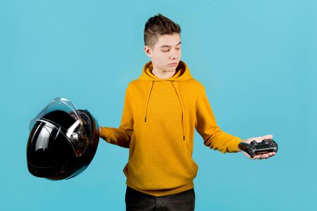 The teenager holds a modified joystick without identification marks and a motorcycle helmet in his hands, choosing a joystick. The choice between real danger and virtualの写真素材
