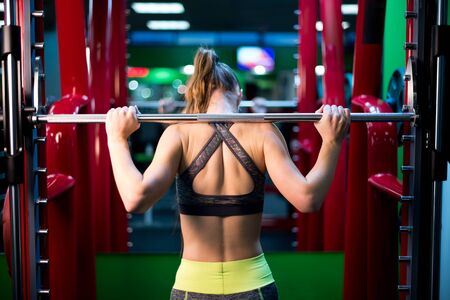 girl is preparing to make an approach in a squat machine, view from the back