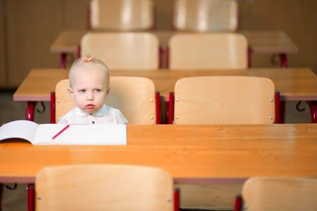 Little preschool girl sits at her desk in the classroom and looks very upset