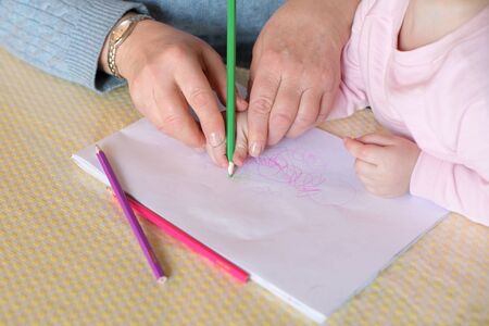 Grandmother teaches little granddaughter to draw. She takes a child s hand and draws out patterns with a pencil, close-up without facesの写真素材