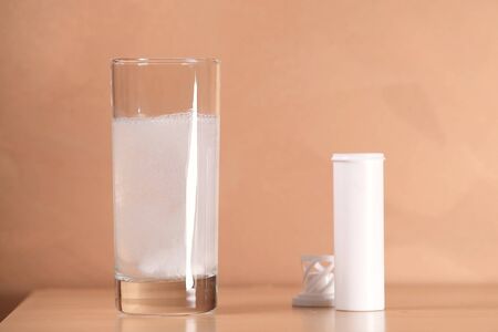 On the bedside table is a glass in which an aspirin tablet is dissolved. Near an open pack of pills and one pill lies on the tableの写真素材