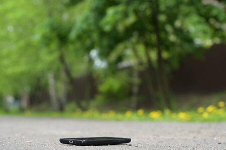 Lost smartphone lies on the asphalt path in the park