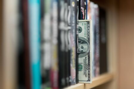 A stack of dollar bills sticking out of a bookshelf. Close up, selective focusの写真素材
