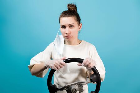 Young woman wipes the steering wheel of a car on a blue background with disinfectant wipesの写真素材