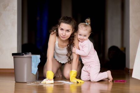 A little sly girl hugs her mother, who launders baby pranks from the floor in their house.の写真素材