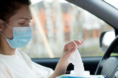 hand in a medical mask pulls an antiseptic napkin from a pack while sitting in a car. Close upの写真素材