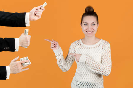 The girl joyfully points to the men's hands that hold out her money. Isolated on a yellow background. Sponsors girls, wealthy boyfriendsの写真素材