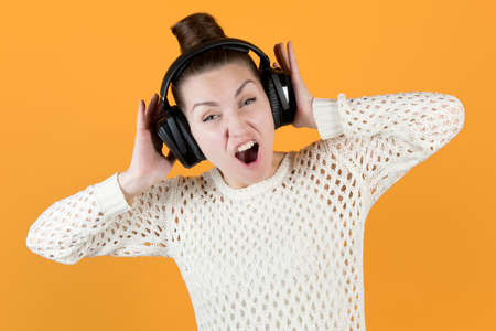 girl screaming holding big headphones on her head, isolated on orange-yellowの写真素材
