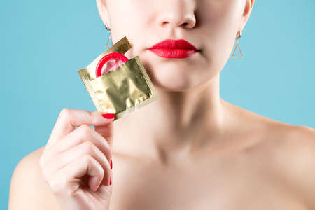a girl with red lips and red nails holds an open red condom near her face. Close-upの写真素材