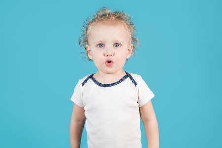 Cute curly baby girl of two years raises folds her lips in a straw on a blue background. Isolated on blueの写真素材