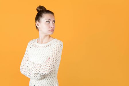 girl with resentment looks at someone over her shoulder, hands clasped on her chest. Isolated on orange-yellow backgroundの写真素材
