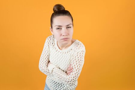 the girl looks suspiciously and squints, clasped her hands on her chest. Wide angle isolated on orange-yellow backgroundの写真素材