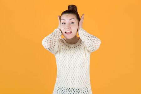 the girl covers her ears with her hands, not wanting to listen to anything, looks at the camera. Isolated on orange-yellowの写真素材
