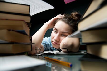 The young woman is tired of studying and bored sleepily at the table, falls asleepの写真素材