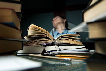 A young student or schoolgirl leaned back in her chair while studying. Selective focus on open book and glasses.の写真素材