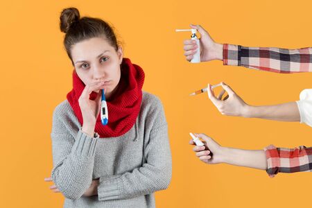 A sick girl with a thermometer in her mouth is offered an injection of medicine, a spray for the...