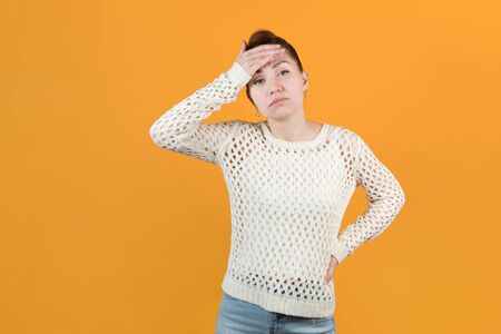 a sickly-looking girl clings to her head. A girl with a sore head is waiting for help and looks hopefully at the camera. Isolated on yellow backgroundの写真素材