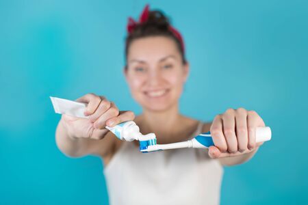 A young woman squeezes toothpaste onto a brush that she is holding in front of herself. Close-up, selective focus. isolated on blueの写真素材