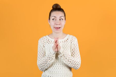 A young girl looks slyly, rubbing her hands and sticking out her tongue. Isolated on a yellow backgroundの写真素材