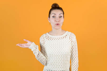 girl holds out his hand to the side, taking something and expresses pleasant surprise. Isolated on orange-yellow backgroundの写真素材
