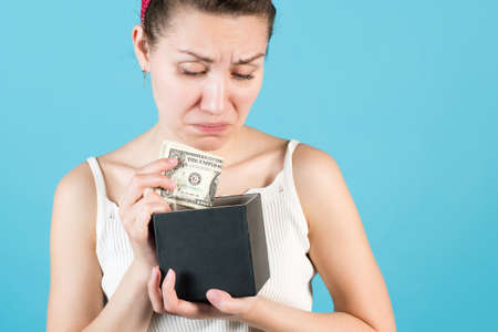 Close-up of a girl who puts or takes dollars out of a piggy bank box. Isolated on blue background.の写真素材