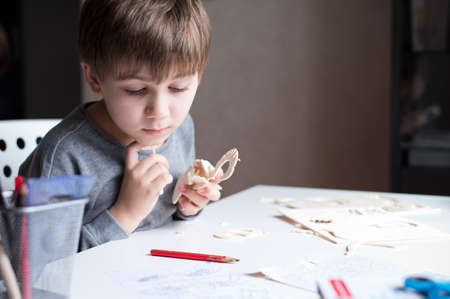 The child collects a wooden craft from parts, sitting in his room. Boy and constructor