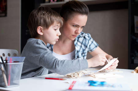 Mom helps her son make a wooden toy from a construction set. Woman and her child, leisureの写真素材