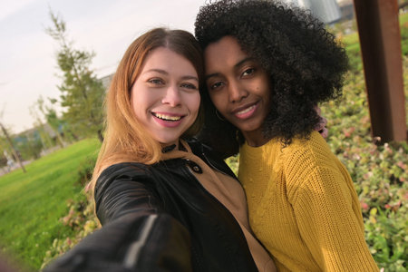 Two young women are taking a selfie, the view from the face of the camera, which is being shot. Multi-ethnic coupleの写真素材