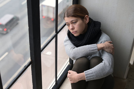 A sad young woman, a resident of the city, leaned her head against the window and looks with sadness at the passing carsの写真素材