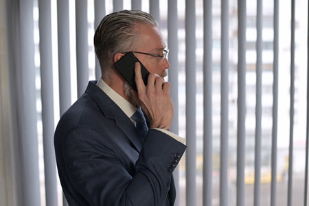 Close-up of a gray-haired executive who speaks on the phone near the window in his officeの写真素材