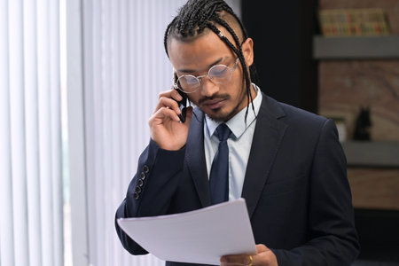 A young black manager looks at work papers and calls on the phone to resolve work issuesの写真素材