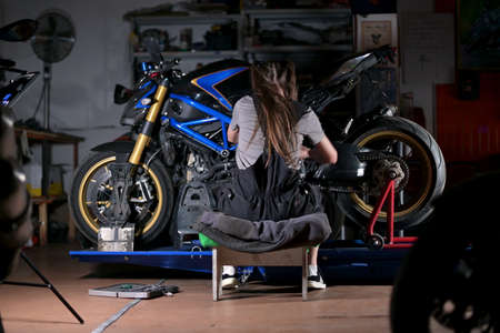 young woman from behind. Woman enthusiastically repairs motorcycle in serviceの写真素材