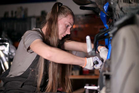 Young woman with a dirty face repairs a motorcycle in a motorcycle service. Selective focusの写真素材