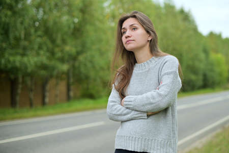 Close-up of a young woman waiting for a ride on a deserted country roadの写真素材