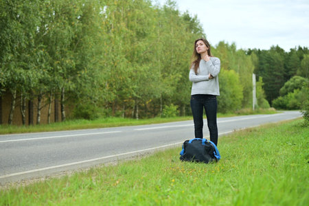 Young pregnant woman waiting for transport on the side of the road with a travel bag. Woman waiting for a bus or a ride outside the cityの写真素材