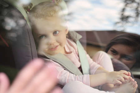 The child looks at his mother from the car and says goodbye, putting his hand to the glass. A touching farewell sceneの写真素材