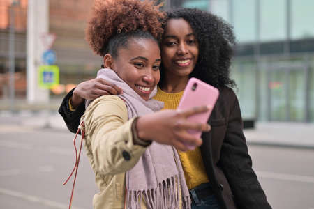 Two smiling young women take a selfie on the background of city landscapes