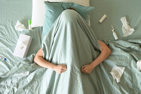 Young sick woman lies in bed with medicines, covered with a blanketの写真素材