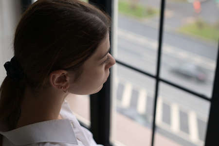 A young woman looks out of the window at passing cars on the road near her houseの写真素材