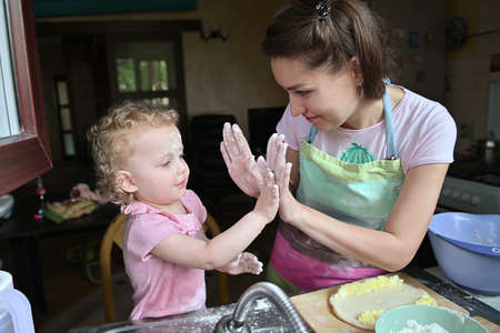 Mom with her little daughter have fun preparing dinner in the kitchen