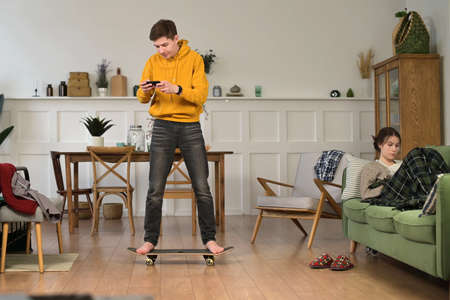 Young funny man at home learning to stand on a skateboard and falls