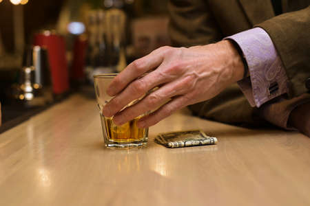 A bar visitor pays for the drink in cash. Close-up of exchanging whiskey for dollarsの写真素材